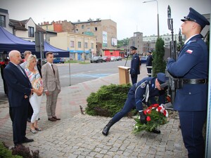 Tata poległego policjanta wraz z rodziną składają kwiaty pod pomnikiem, przed budynkiem komendy.