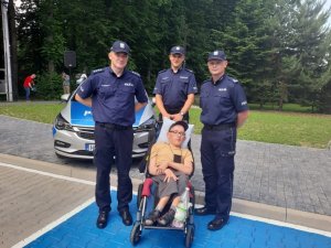 Trzech policjantów stoi razem z niepełnosprawnym chłopakiem na wózku.