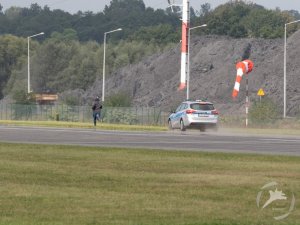 Policyjny radiowóz ściga osobę biegnącą pasem startowym lotniska.