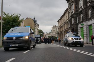 Dwa policyjne radiowozy jada prowadząc marsz ulicą