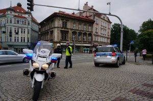 Na pierwszym planie motocykl z ruchu drogowego, w tle policjanci stoją przy skrzyżowaniu.