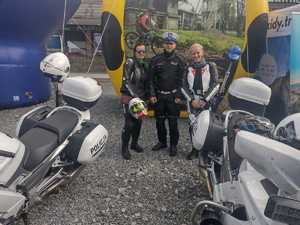 Policjant pozuje do zdjęcia z dwiema motocyklistkami, obok policyjne motocykle.