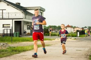 Podkomisarz Dariusz Stypułkowski biegnie wraz ze swoim synem. W tle widać zabudowania.