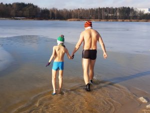 Podkomisarz Dariusz Stypułkowski wraz z synem, którego trzyma za rękę wchodzą do zalewu wodnego na Łysinie w Bieruniu. Obaj są w kąpielówkach i czapkach