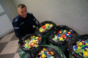 Na korytarzu komendy policjant kuca przy workach z kolorowymi, plastikowymi nakrętkami