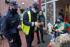 Przed wejściem do przedszkola policjant i strażnik miejski wręczają dzieciom odblaski