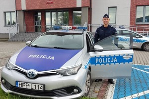 Policjant stojący przy radiowozie na tle Komendy Powiatowej Policji w Bieruniu.