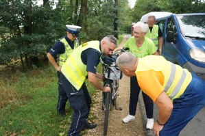 Na zdjęciu widzimy policjanta jak pomaga kobiecie, której popsuł się rower