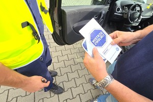 Na zdjęciu widzimy policjanta oraz kierującego z ulotkami oraz naklejką Mistrzu Zwolnij
