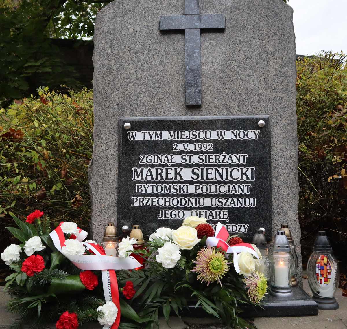 Zdjęcie przedstawia tablicę upamiętniającą tragiczną śmierć starszego sierżanta Marka Sienickiego oraz złożone kwiaty i znicze.