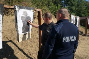 Instruktor strzelania przy tarczy omawia z policjantem wyniki jego strzelania