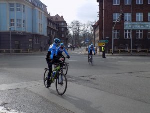 3 rowerzystów uczestniczących w zawodach jadących ulicami miasta w trakcie biegu