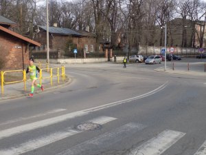 zawodnik biegnący ulicami miasta, w tle policjant drogówki zabezpieczający skrzyżowanie