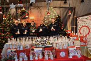 Zdjęcie przedstawia policjantów, którzy trzymają zapakowane aniołki, stoją pośród prezentów i udekorowanych choinek.