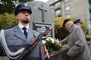 Zdjęcie przedstawia miejsce tragicznej śmierci policjanta, wartę honorową i ojca policjanta, który stawia znicz.