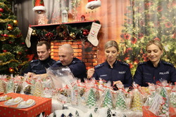 Zdjęcie przedstawia scenerię świąteczną i pakujących prezenty policjantów.