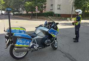 Na zięciu policjant obok motocykl służbowy.