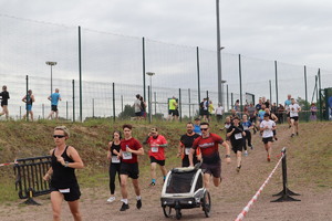 Na zdjęciu biegnący uczestnicy, wśród nich mężczyzna biegnący z dzieckiem w wózku