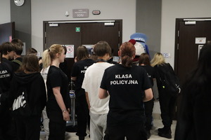 Na zdjęciu na korytarzu stojące osoby, obok nich policyjna maskotka, osoba przebrana za niebieskiego psa Sznupka.
