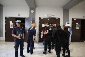 Na zdjęciu na korytarzu stojące osoby, obok nich policjant i dwie policjantki oraz osoba przebrana za niebieskiego psa Sznupka.