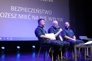 Na zdjęciu, na cenie trzech siedzących policjantów, siedzący pośrodku przemawia do mikrofonu
