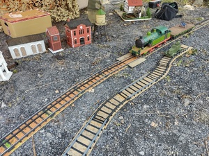 Na zdjęciu mała lokomotywa znajdująca się na małych torach, obok małe domki.