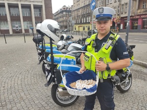 Na zdjęciu policjant trzymający koszyk z ciastkami, za nim trzy motocykle służbowe.