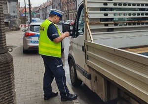 Na zdjęciu policjant stojący przy samochodzie, za nim radiowóz.
