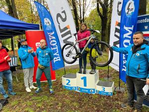 Na zdjęciu kobieta trzymająca w rękach rower i chłopiec stojący na 1 miejscu podium.