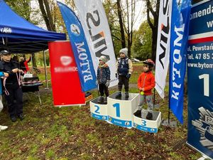 Na zdjęciu trójka dzieci stojących na podium obok policjantka z medalami.