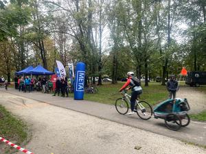 Na zdjęciu rowerzysta jadący z przyczepką rowerową, przed nim meta i zgromadzone osoby.