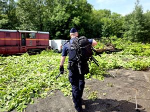 na zdjęciu policjant z plecakiem na ramieniu idący w stronę pojazdów znajdujących się na torowisku.
