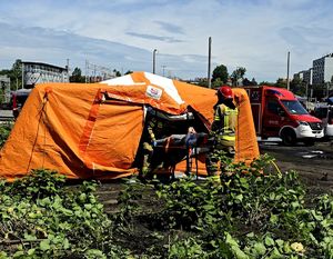 na zdjęciu namiot pomarańczowego koloru, strażacy wnoszący do niego osobę na noszach