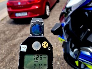 na zdjęciu urządzenie pomiarowe, wynik 126, obok policyjny motocykl i czerwony seat