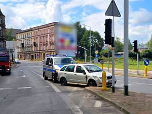 na zdjęciu na jezdni samochód osobowy koloru szarego za nim policyjny radiowóz.