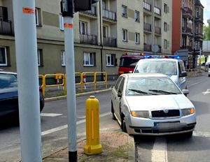 na zdjęciu na jezdni samochód osobowy koloru szarego za nim policyjny radiowóz.