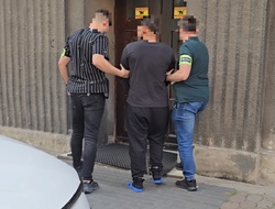 na zdjęciu zatrzymany mężczyzna wprowadzany do budynku prokuratury przez dwóch nieumundurowanych policjantów