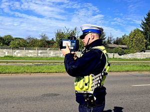 na zdjęciu policjant stojący na drodze i wykonujący pomiar prędkości
