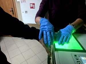 dłoń mężczyzny na urządzeniu do pobierania śladów daktyloskopijnych trzymana przez dłonie w niebieskich rękawiczkach