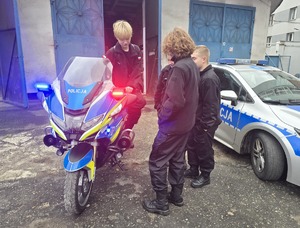 na zdjęciu trzech uczniów przy motocyklu służbowym, obok radiowóz