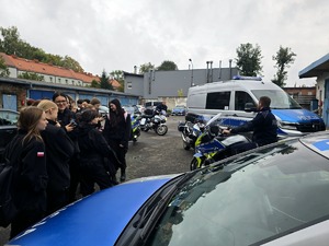 na zdjęciu na zewnątrz budynku pojazdy służbowe, motocykle służbowe przy nich uczniowie klasy mundurowej i policjanci