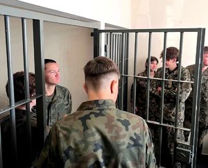 na zdjęciu licealiści przy kratach, w pomieszczeniu dla zatrzymanych osób