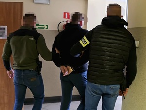na zdjęciu zatrzymany mężczyzna prowadzony przez dwóch nieumundurowanych policjantów