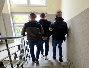 na zdjęciu zatrzymany mężczyzna prowadzony po schodach przez dwóch nieumundurowanych policjantów