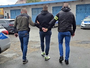 na zdjęciu zatrzymany mężczyzna prowadzony przez dwóch nieumundurowanych policjantów