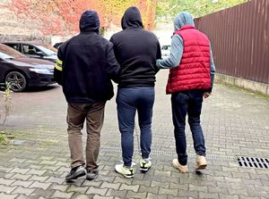 na zdjęciu zatrzymany mężczyzna prowadzony przez dwóch nieumundurowanych policjantów