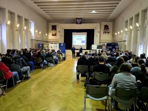 na zdjęciu uczniowie siedzący na krzesłach w sali przed nimi policjant