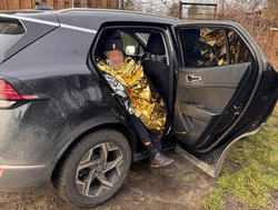 Na zdjęciu mężczyzna siedzący w samochodzie przy otwartych drzwiach, przykryty folią złotego koloru