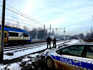 policjant i funkcjonariusz Straży Ochrony Kolei przy torowisku, obok radiowóz policyjny, na torach pociąg
