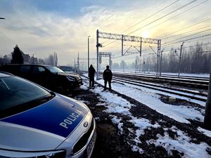 policjant i funkcjonariusz Straży Ochrony Kolei przy torowisku, obok radiowóz policyjny